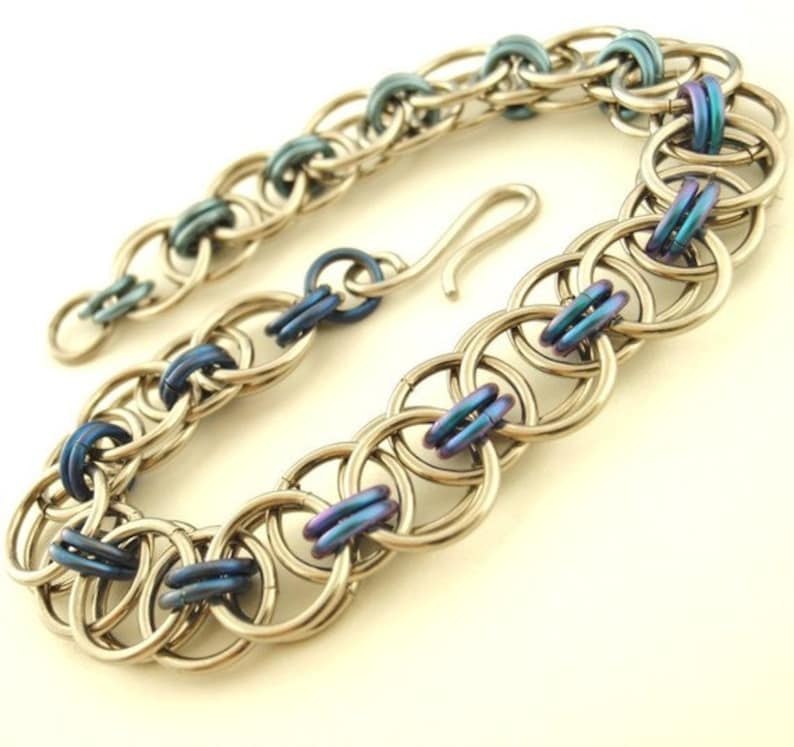 May include: A silver and blue chain bracelet with a hook clasp. The bracelet is made of small metal rings that are linked together.