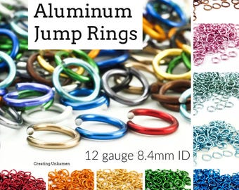 Puede incluir: Una colección de anillas de salto de aluminio en varios colores, incluyendo rojo, azul, verde, oro, naranja y marrón. El texto Aluminum Jump Rings y 12 gauge 8.4mm ID es visible. Estos anillos metálicos se muestran en varios montones.