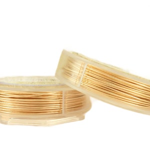 May include: Two spools of thin, metallic gold-colored craft wire wound tightly around clear plastic circular bobbins. The wire is smooth and reflective, creating a uniform coil pattern on each spool. The spools are positioned slightly overlapping.
