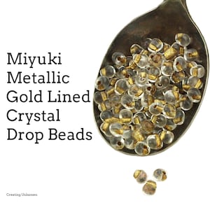Puede incluir: Una cuchara llena de cuentas de cristal transparente con detalles dorados. Las cuentas se llaman "Miyuki Metallic Gold Lined Crystal Drop Beads".