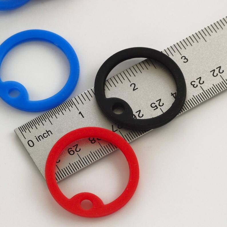 May include: Three silicone key rings in red, blue, and black. The rings are 1 inch in diameter and have a small hole in the center. The rings are shown on a ruler.