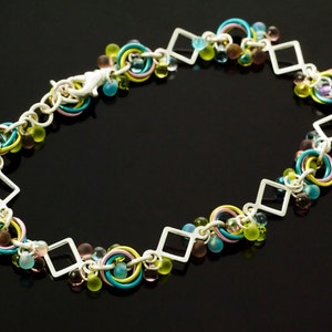 May include: A silver chain necklace with a variety of colorful glass beads, including green, blue, pink, and purple. The chain is made of small squares and circles.