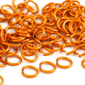 May include: A large pile of orange jump rings. The rings are made of metal and are all the same size. They are ideal for jewellery making or other crafts.