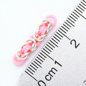 K&ouml;nnte beinhalten: Ein rosafarbenes und silbernes Gliederarmband mit einer L&auml;nge von etwa 1 cm.
