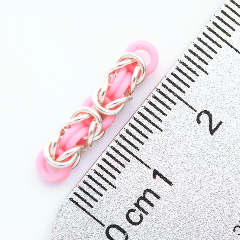 K&ouml;nnte beinhalten: Ein rosafarbenes und silbernes Gliederarmband mit einer L&auml;nge von etwa 1 cm.