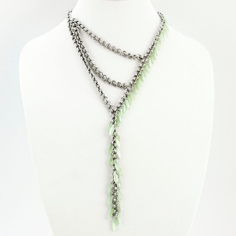 Puede incluir: Un collar de cadenas m&uacute;ltiples en tono plateado con un dise&ntilde;o en forma de Y. El collar est&aacute; adornado con numerosas cuentas peque&ntilde;as, transl&uacute;cidas y en forma de hoja de color verde menta p&aacute;lido, fijadas a lo largo de un lado de las cadenas.