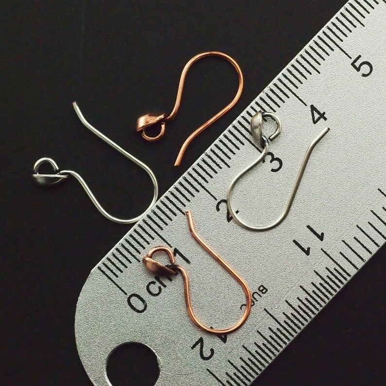 May include: Three earring hooks, one silver, one copper, and one gold, are laid out on a ruler. The ruler is marked in centimeters and inches.