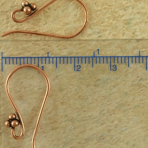 May include: Two copper earring hooks with a cluster of three small copper beads at the top of each hook. The hooks are approximately 1 inch long.