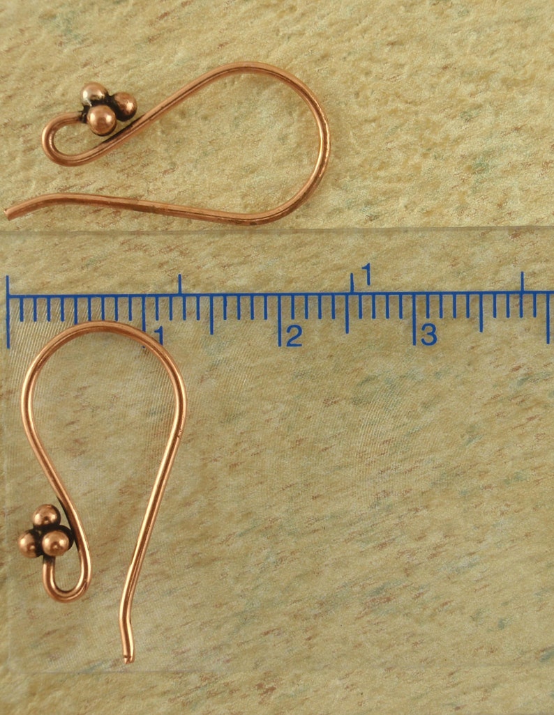 May include: Two copper earring hooks with a cluster of three small copper beads at the top of each hook. The hooks are approximately 1 inch long.