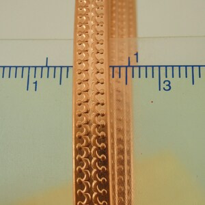 May include: Close-up of a gold-coloured metal bangle with a decorative pattern. The bangle is approximately 2.5 cm wide and has a smooth, polished finish.