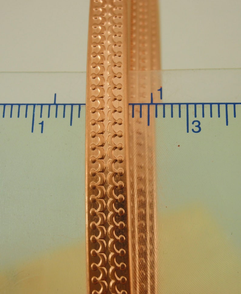 May include: Close-up of a gold-coloured metal bangle with a decorative pattern. The bangle is approximately 2.5 cm wide and has a smooth, polished finish.