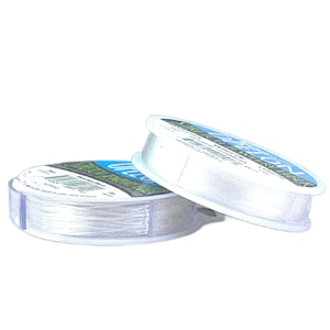 May include: Two clear plastic spools of Stretch Magic jewelry cord. Each spool features a blue and green label with the text Stretch Magic and Elastic Cord. The transparent, thin, flexible cord is wound tightly around the center of each spool.