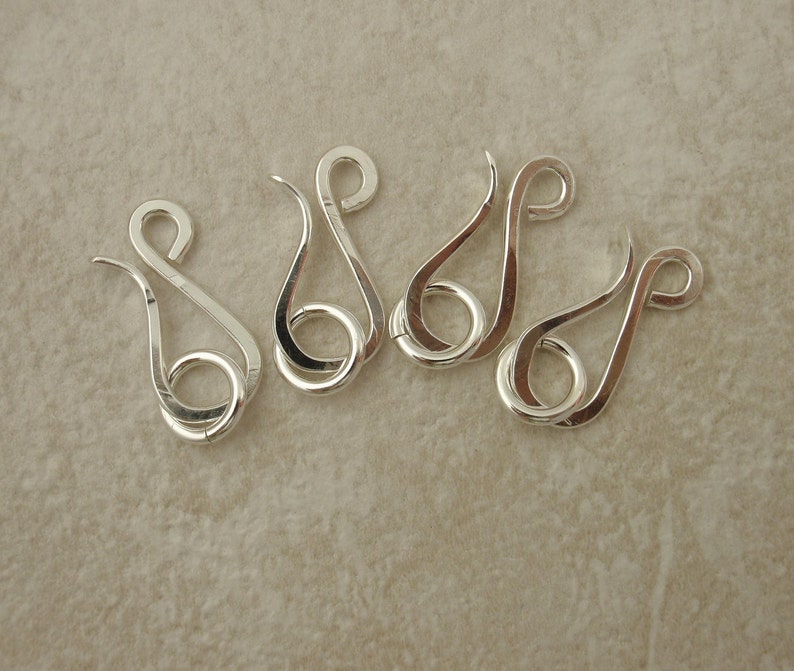 K&ouml;nnte beinhalten: F&uuml;nf silberfarbene Metallhaken mit einem einzigartigen geschwungenen Design. Jeder Haken hat eine kleine Schlaufe am Ende.