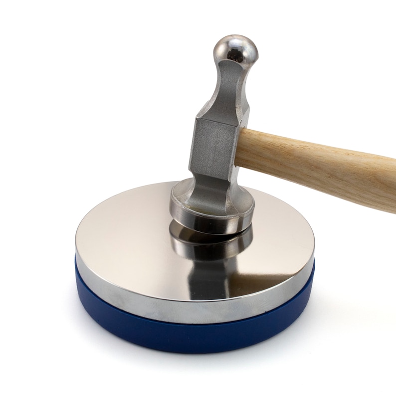 May include: A metal forming set with a polished steel disc and a ball-peen hammer. The disc has a blue base and the hammer has a wooden handle. The tools are designed for shaping and forming metal.