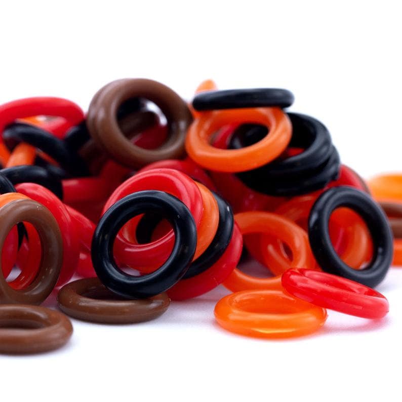 K&ouml;nnte beinhalten: Ein Haufen bunter Gummringe in Schwarz, Braun, Orange und Rot. Die Ringe sind alle unterschiedlich gro&szlig; und in einem zuf&auml;lligen Muster angeordnet.