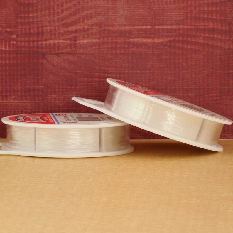 May include: Two spools of clear elastic thread, wound on white plastic spools with a label that reads "Elastic Thread".