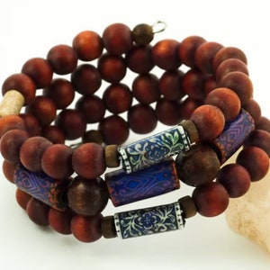 May include: A triple-strand bracelet made of dark brown wooden beads with blue and white patterned accents.