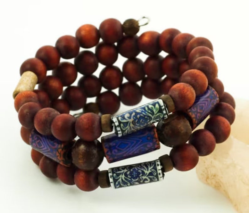 May include: A triple-strand bracelet made of dark brown wooden beads with blue and white patterned accents.