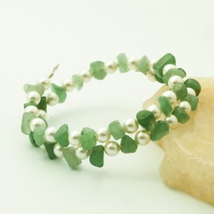 May include: A double-strand bracelet made with green jade and white pearls. The bracelet is wrapped around a light brown rock.