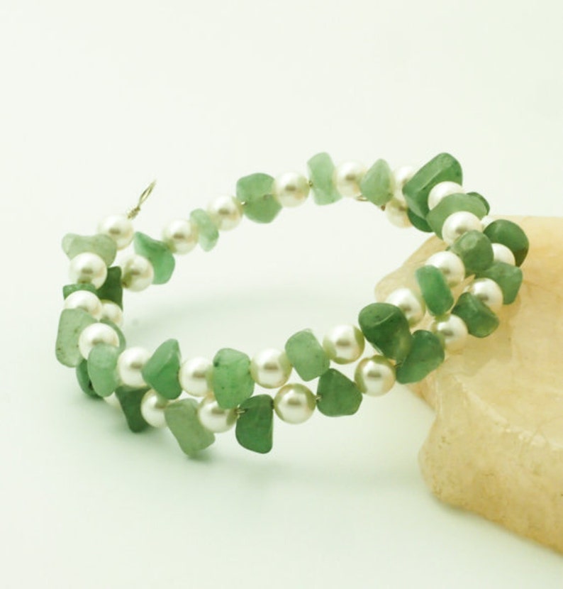 May include: A double-strand bracelet made with green jade and white pearls. The bracelet is wrapped around a light brown rock.