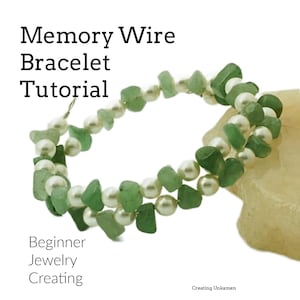 May include: A green and white memory wire bracelet with green stone beads and white pearl beads. The bracelet is on a light brown surface. Memory Wire Bracelet Tutorial.