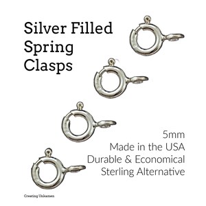 Puede incluir: Primer plano de cierres de resorte plateados, de 5 mm. Los cierres son circulares con una pequeña palanca. La imagen incluye texto que indica que están hechos en los EE. UU. y son una alternativa duradera y económica a la plata de ley.