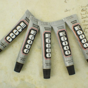 May include: Five tubes of E6000 industrial strength adhesive. Each tube is labeled with the brand name and strength. The tubes are silver with black lettering.