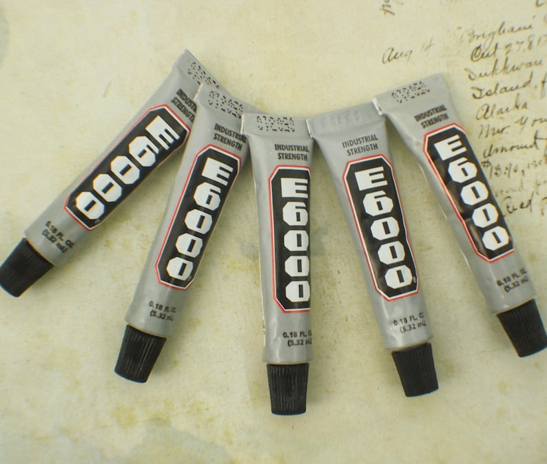 May include: Five tubes of E6000 industrial strength adhesive. Each tube is labeled with the brand name and strength. The tubes are silver with black lettering.