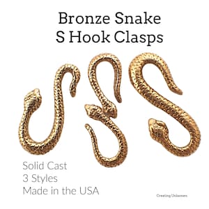 May include: Three gold-colored snake-shaped S hook clasps. The clasps are solid cast and come in three styles. The text "Bronze Snake S Hook Clasps" and "Solid Cast 3 Styles Made in the USA" is visible in the image.