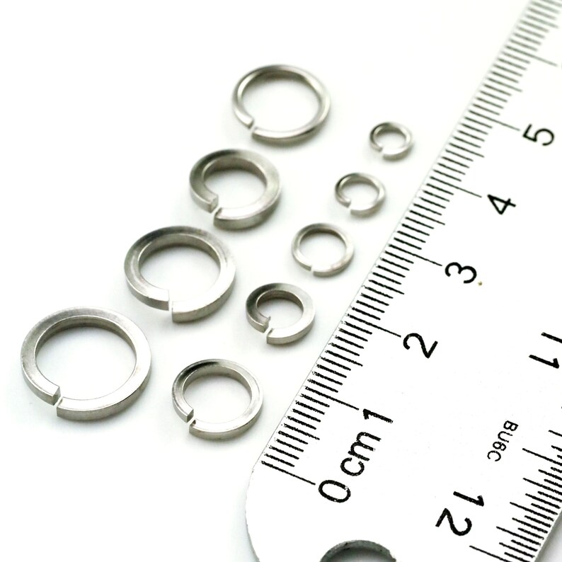 Puede incluir: Surtido de anillos de salto de metal plateado de diferentes tama&ntilde;os, medidos con una regla en cent&iacute;metros.