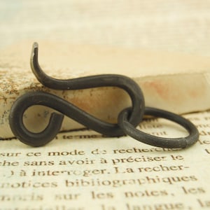Puede incluir: Un gancho de metal negro con un diseño único en forma de S. El gancho está hecho de metal forjado y tiene un aspecto rústico y antiguo.
