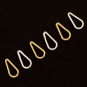 May include: Seven teardrop-shaped hoops in gold and silver. The hoops are arranged in a row, with the gold hoops alternating with the silver hoops.