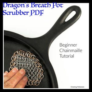 Puede incluir: Primer plano de una sartén de hierro fundido negra con un estropajo de malla de cadena plateada y cobre apoyado en la superficie. El texto "Dragon's Breath Pot Scrubber PDF" y "Beginner Chainmaille Tutorial" es visible en la imagen.