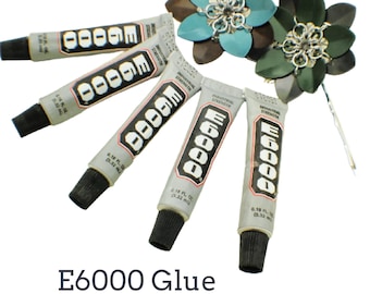 May include: Five tubes of E6000 industrial strength adhesive, each containing 0.18 fluid ounces, arranged in a fan shape next to two decorative metal flower hair pins with teal and dark green petals and silver-toned chainmail centers.