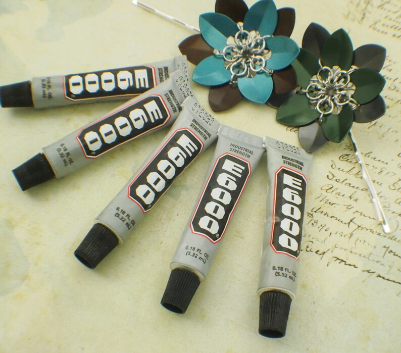 May include: Five tubes of E6000 industrial strength adhesive, each with a black cap and a silver label with the text "E6000 Industrial Strength" and "0.18 fl oz (5.32 ml)".