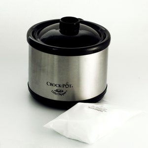 May include: A silver Crock-Pot Little Dipper slow cooker with a black lid. The slow cooker is on a white surface.