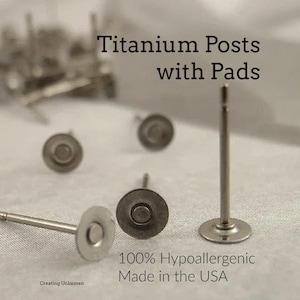 May include: Silver-toned metal earring components featuring flat circular pads and straight posts. The text on the image reads: Titanium Posts with Pads, 100% Hypoallergenic, Made in the USA, and Creating Unkamen. These are jewelry findings.