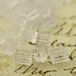 May include: Close-up of a group of clear plastic earring backs. The backs are designed with a star-shaped center and ridges around the outside.