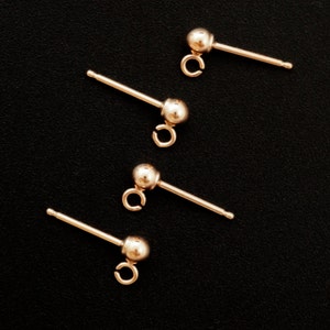 May include: Four gold-toned earring findings with a small ball at the end and a loop for attaching jewelry.