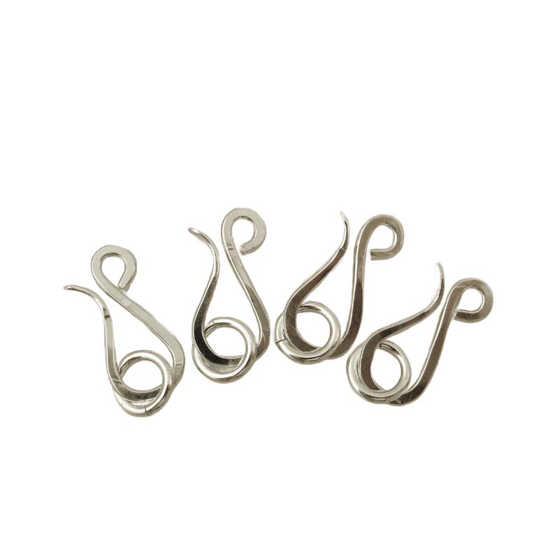 K&ouml;nnte beinhalten: F&uuml;nf silberfarbene Metallverschl&uuml;sse mit einem einzigartigen, geschwungenen Design. Jeder Verschluss hat an einem Ende eine Schlaufe und am anderen Ende einen Haken.
