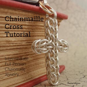 Puede incluir: Un colgante de cruz de malla de cadena plateada, hecho con el tejido persa completo, cuelga de un libro. El texto "Chainmaille Cross Tutorial" es visible sobre el colgante. El texto "Intermediate Full Persian Chainmaille Jewelry" es visible debajo del colgante.