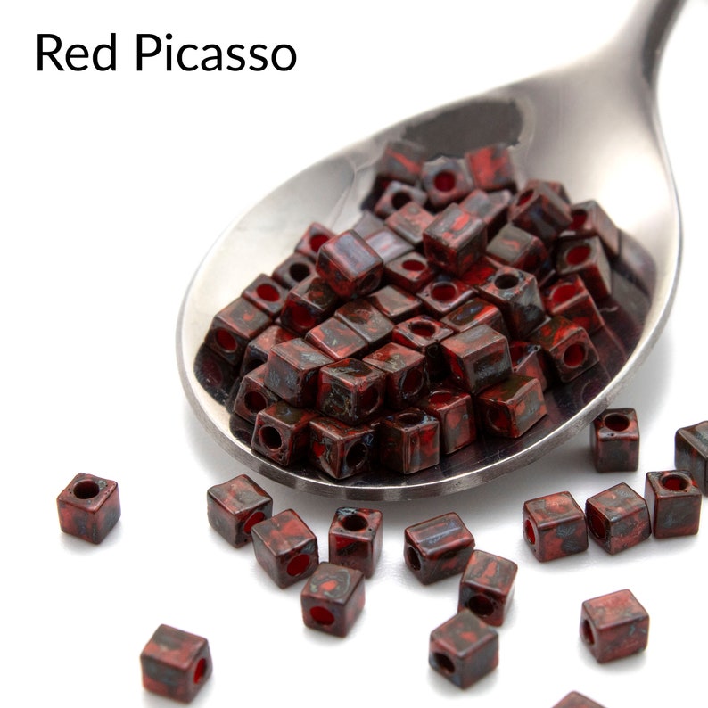 May include: Red Picasso square glass beads in a silver spoon. The beads are a mix of red and black with a speckled finish.
