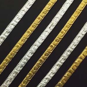May include: Five strips of decorative trim, two gold and three silver, with a floral pattern. The trim is arranged diagonally on a black background.