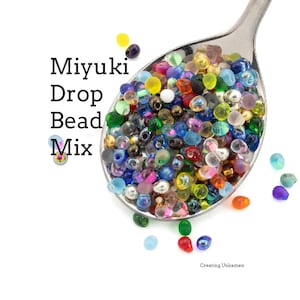 May include: A stainless steel spoon filled with a colorful mix of Miyuki drop beads. The beads are in various colors, including blue, green, yellow, and pink. The text "Miyuki Drop Bead Mix" is displayed on the left side of the image.