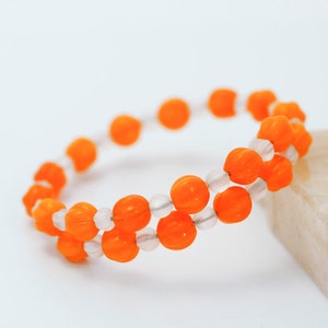 May include: A bracelet made of orange and white beads. The orange beads are shaped like pumpkins.