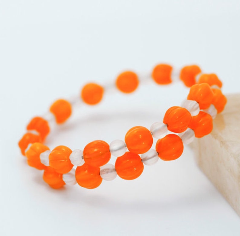 May include: A bracelet made of orange and white beads. The orange beads are shaped like pumpkins.