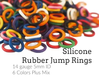 May include: A pile of multicolored silicone rubber jump rings in orange, blue, yellow, red, green, and white. The text reads: Creating Unkamen, Silicone Rubber Jump Rings, 14 gauge 5mm ID, 6 Colors Plus Mix. These rings are circular and flexible.