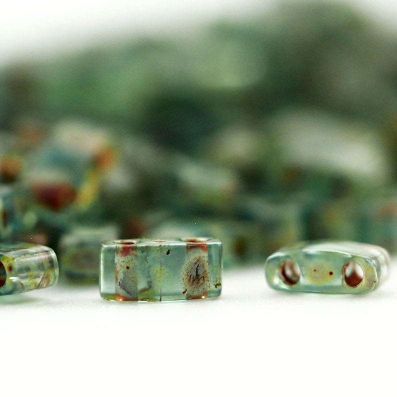 May include: A collection of rectangular glass beads featuring a translucent light green base with mottled brown and rust-colored inclusions. Each bead is shaped as a flat, elongated rectangle with two circular holes drilled horizontally through the center.