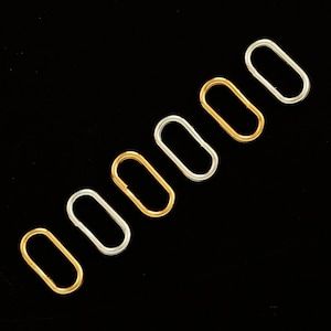 Könnte beinhalten: Sieben ovale Metallringe in verschiedenen Größen, diagonal angeordnet. Die Ringe sind silber und goldfarben.