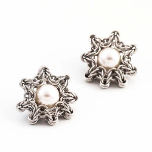K&ouml;nnte beinhalten: Ein Paar silberne Ohrringe mit einem sternf&ouml;rmigen Design und einer wei&szlig;en Perle in der Mitte jedes Sterns.